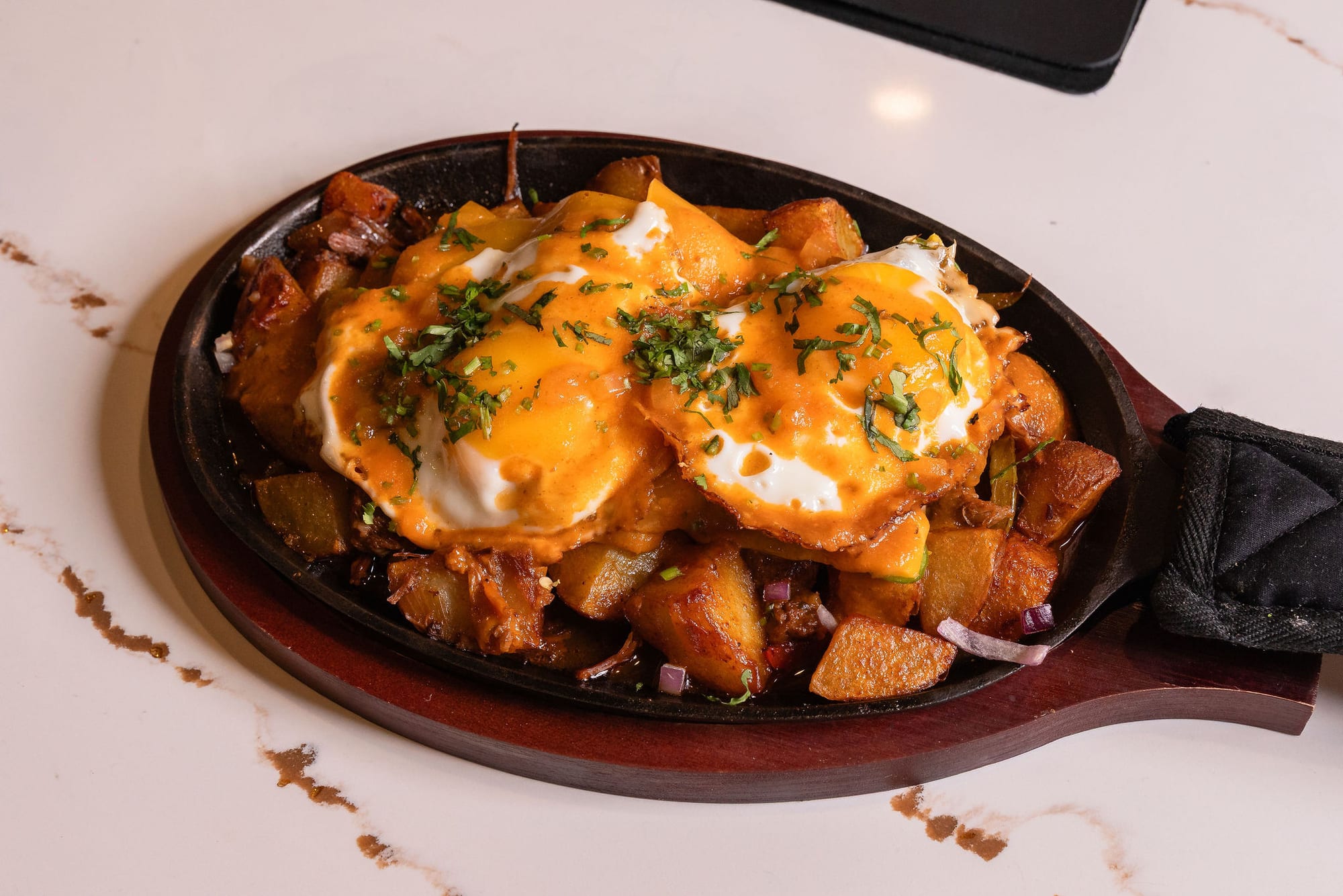 A cast-iron breakfast skillet — potatoes, melted cheese, and eggs with herbs
