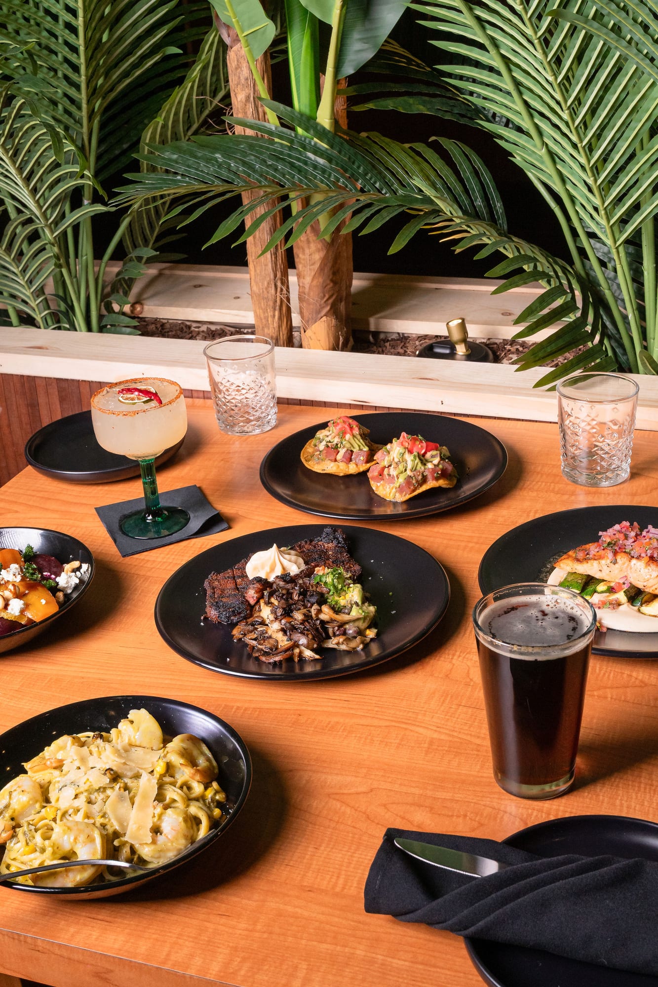 A dinner spread with a margarita, steak, tostadas, and shared plates