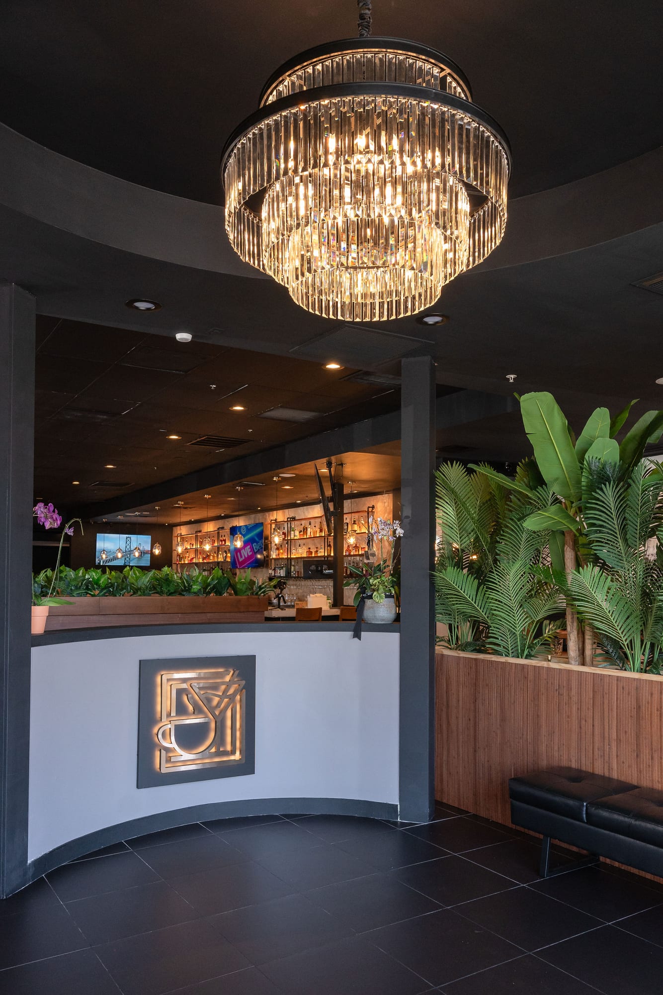 The dining room and bar beneath a crystal chandelier, framed by tropical plants