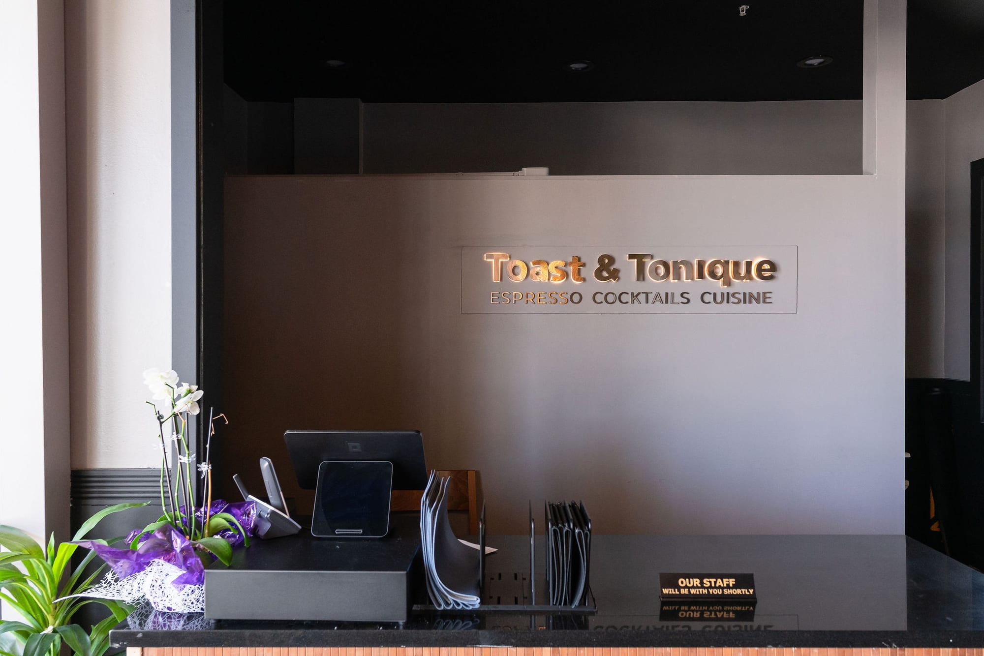 The host stand beneath the Toast & Tonique sign, with fresh orchids