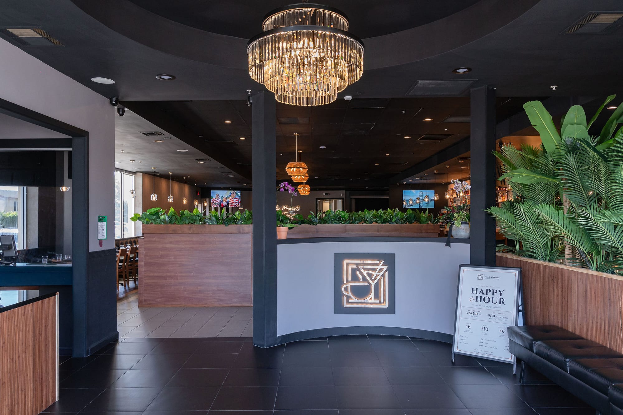 The entrance beneath the chandelier with the monogram and a Happy Hour sign