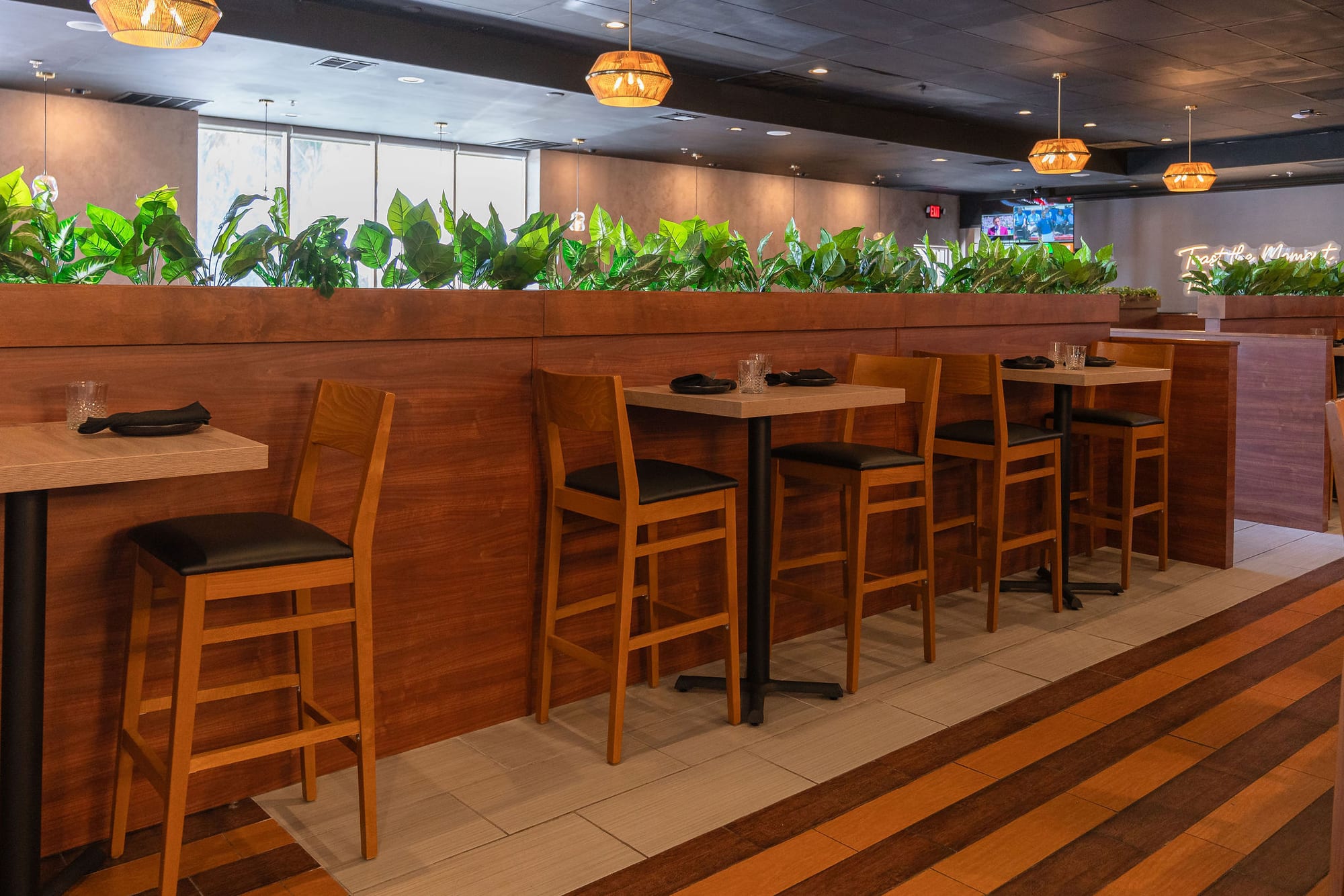 High-top wood tables beside a planter divider on striped wood floors
